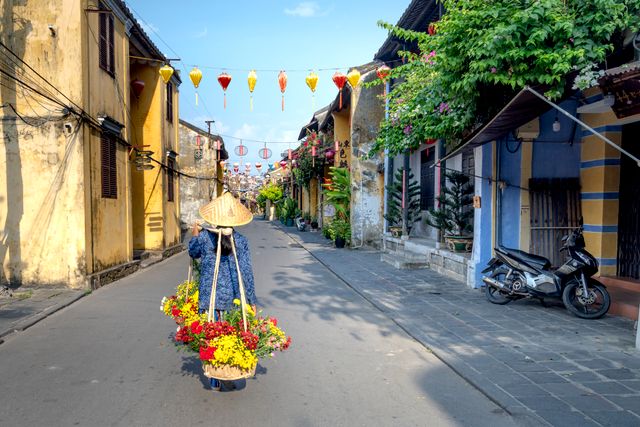 A street vendor carrying flowers through a lantern-lined street in Hội An